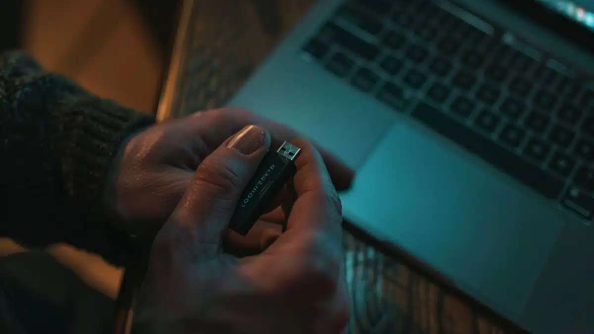 Person holding USB drive next to laptop.